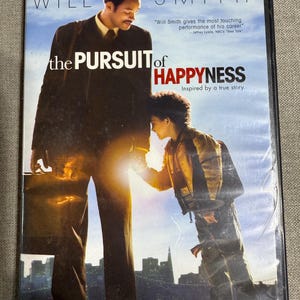 May include: DVD of the movie "The Pursuit of Happyness" featuring Will Smith. The cover art shows Smith with a child, with the title in large, bold letters. The DVD case is in a plastic sleeve.