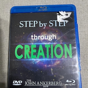 Puede incluir: Una caja Blu-ray azul con el título "STEP by STEP through CREATION" en letras blancas y verdes. La caja presenta un logotipo de DVD y el texto "The John Ankerberg Show". El fondo muestra una imagen de galaxia.
