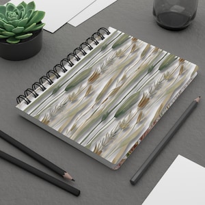 May include: A spiral bound notebook with a white cover featuring a repeating pattern of green, brown, and beige watercolor leaves and stems.