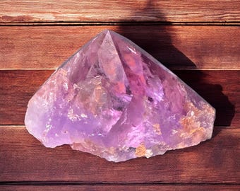 May include: A large, faceted amethyst crystal with shades of purple and hints of orange and brown. The crystal is set against a wooden background.