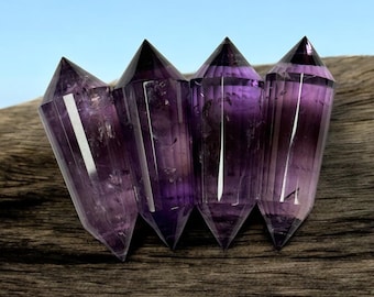 May include: Five amethyst crystal points, each with a pointed tip and a faceted, clear body, arranged in a row on a dark brown wooden surface.
