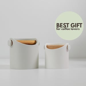 Puede incluir: Dos accesorios de café cilíndricos blancos con asas y detalles de madera. El texto "BEST GIFT for coffee lovers" está en un círculo verde. Los accesorios son de diferentes tamaños.