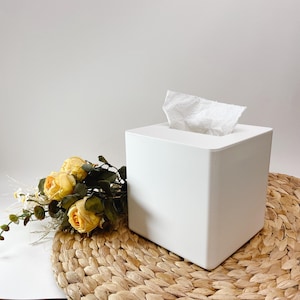 Peut inclure: Un porte-mouchoirs carré blanc avec un mouchoir blanc à l'intérieur. Le porte-mouchoirs est posé sur un tapis de paille tressé avec un bouquet de roses jaunes.