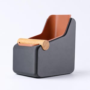 Puede incluir: Un organizador de escritorio moderno y minimalista con forma de silla. El exterior es negro mate, con un interior marrón cálido y un asa de madera natural. Ideal para guardar bolígrafos, lápices o pequeños útiles de oficina. Dimensiones: aproximadamente 15 cm x 15 cm x 15 cm.
