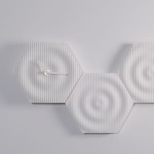 Puede incluir: Un reloj de pared moderno compuesto por tres baldosas hexagonales blancas. La esfera del reloj presenta un patrón texturizado de rayas verticales y manecillas doradas. El diseño es minimalista y contemporáneo, adecuado para la decoración del hogar.