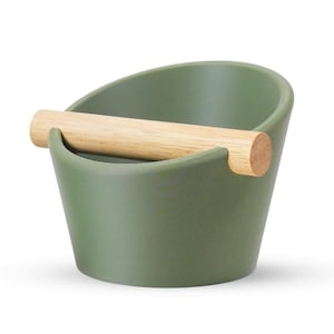 Può includere: Un contenitore per bussare il caffè in ceramica verde con un manico in legno naturale. Il contenitore ha un design curvo e viene utilizzato per smaltire le pastiglie di caffè espresso. Il manico è di colore marrone chiaro e di forma cilindrica.