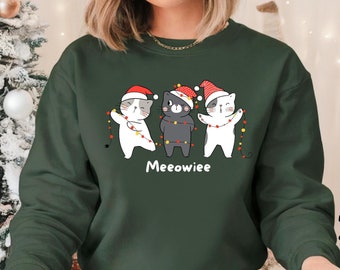 May include: A military green sweatshirt featuring a graphic of three cartoon cats wearing Santa hats and string lights. The word "Meewiee" is printed below the cats. The sweatshirt is available in 6 sizes and 14 colors.