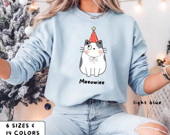 May include: Light blue sweatshirt featuring a cartoon cat wearing a party hat with a star. The cat has gray spots and a bow tie. The word "Meeowiee" is printed below the cat. The text "light blue", "6 sizes", and "14 colors" are also visible.