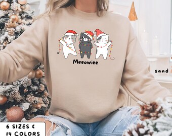 May include: Sand-colored sweatshirt featuring a graphic of three cartoon cats wearing Santa hats and holding Christmas lights. The word "Meeowiee" is printed below the cats. The sweatshirt is available in 6 sizes and 14 colors.