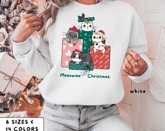 May include: White sweatshirt featuring a graphic of cartoon cats in gift boxes with the text "Meeowiee Christmas". The cats wear Santa hats. The sweatshirt also has the text "white", "6 sizes & 14 colors".