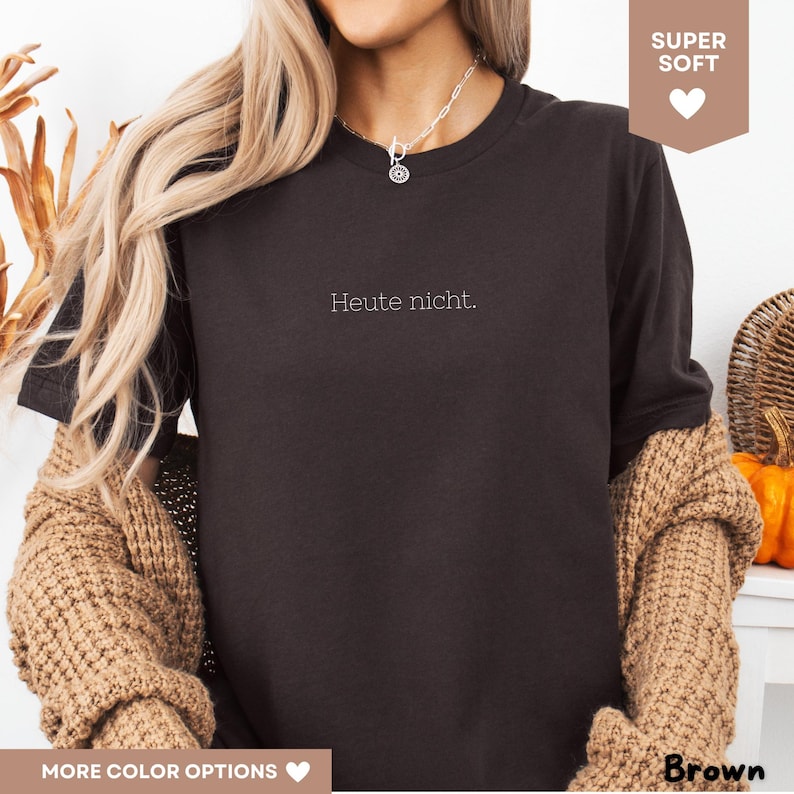 May include: Brown crew neck t-shirt with the phrase "Heute nicht" in white. The shirt is labeled "Super Soft" and "More Color Options". The word "Brown" is also displayed. The model is wearing a brown sweater.