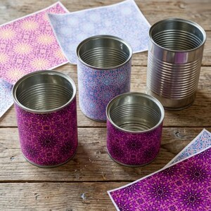 Peut inclure: Trois boîtes de conserve métalliques cylindriques de hauteurs variées, deux enveloppées dans du papier à motifs violets et une dans du papier à motifs bleus, avec une boîte en métal argenté. Des feuilles de papier à motifs sont éparpillées.
