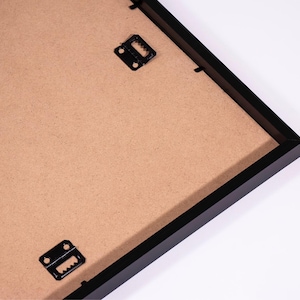 May include: Black picture frame with a brown cardboard backing and two metal hanging clips.