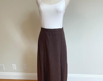 May include: A white sleeveless camisole with thin straps paired with a solid dark brown midi-length skirt. The skirt features a structured waistband and vertical seam detailing that creates subtle pleats, extending down to a straight hemline.