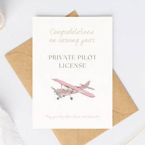 May include: A greeting card with a light beige background and a brown envelope. The card reads "Congratulations on earning your PRIVATE PILOT LICENSE" with a pink airplane illustration. The bottom of the card says "May you have blue skies and tailwinds!"