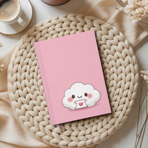 May include: A pink hardback notebook featuring a central illustration of a white, smiling cloud character with rosy cheeks holding a small white envelope decorated with a red heart. The notebook has a smooth, solid pink cover finish.