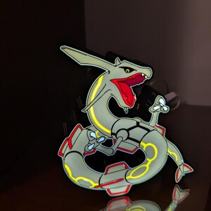 K&ouml;nnte beinhalten: Eine stilisierte, hellgraue Drachenfigur mit gelben und roten Akzenten. Der Drache hat einen langen, gewundenen K&ouml;rper und ein detailliertes Design, mit rotem Maul und gelben Highlights. Wahrscheinlich ein Sammler- oder Dekorationsartikel.