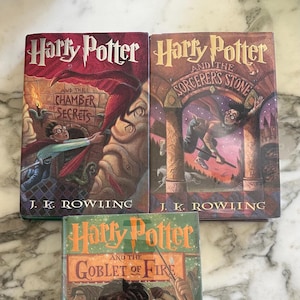 May include: Three hardcover books in a vertical stack. The books are all Harry Potter novels. The top book is "Harry Potter and the Sorcerer's Stone", the middle book is "Harry Potter and the Chamber of Secrets", and the bottom book is "Harry Potter and the Goblet of Fire".