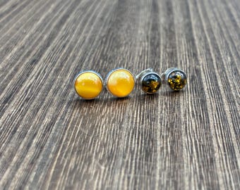 May include: Two pairs of stud earrings featuring round, polished stones set in silver-toned metal. One pair displays bright, opaque yellow stones, while the other pair features darker, translucent amber-colored stones with visible internal inclusions.