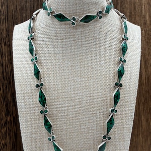 May include: A silver necklace and matching bracelet set featuring elongated diamond-shaped links inlaid with dark green, mottled stone segments. The jewelry pieces are connected by small, circular silver links, creating a continuous, repeating geometric pattern throughout the entire length of both items.