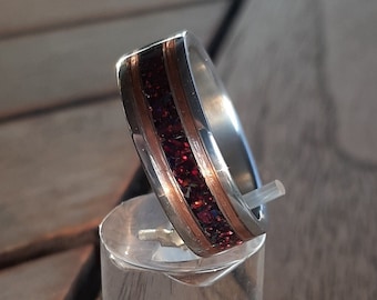 Puede incluir: Un anillo de plata con una banda de piedras preciosas rojas y una incrustación de cobre.