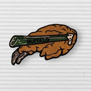 May include: A brown and green embroidered patch with a brain shape and a pencil with the word "BUFFALO" on it.