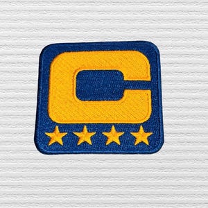 May include: A blue and yellow embroidered patch with a large letter "C" and five yellow stars below it.