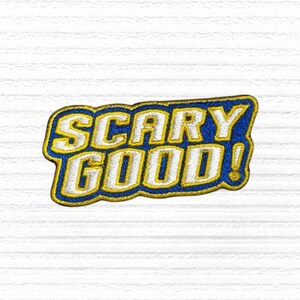 May include: Embroidered patch with the words "SCARY GOOD!" in white, outlined in gold, set against a blue background. The patch has a gold border and is on a white, textured background.
