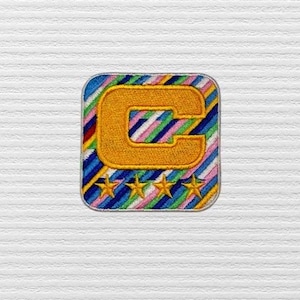 May include: A colorful embroidered patch with a yellow letter "C" and five gold stars. The patch has a striped design with blue, green, pink, and white stripes.