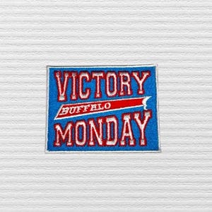 May include: Blue and red embroidered patch with the text "VICTORY MONDAY" and "BUFFALO" in white lettering.