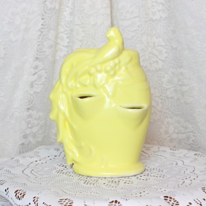 May include: A yellow ceramic vase with a bird and floral design. The vase has two openings for flowers.