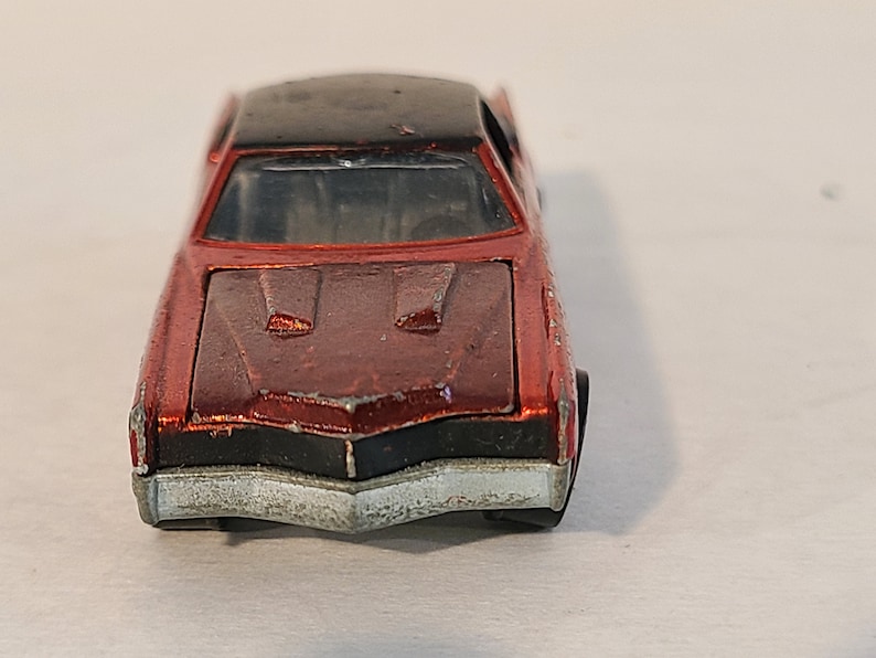 May include: A red toy car with a black roof and a silver front bumper. The car has a detailed hood with two air vents.
