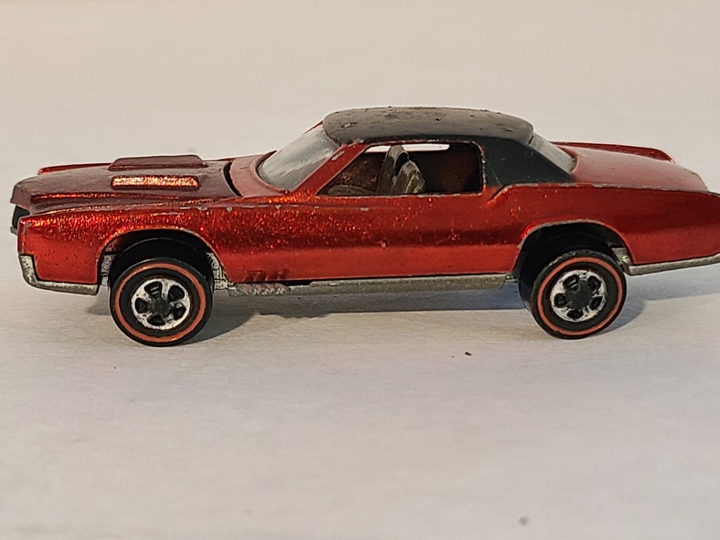 May include: A red toy car with a black roof and chrome accents. The car has a detailed interior and black wheels with red trim.