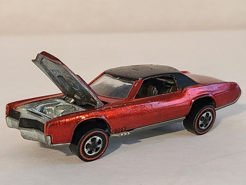 May include: Red die-cast toy car with a black roof and an open hood. The car has a detailed engine and black wheels with red trim.