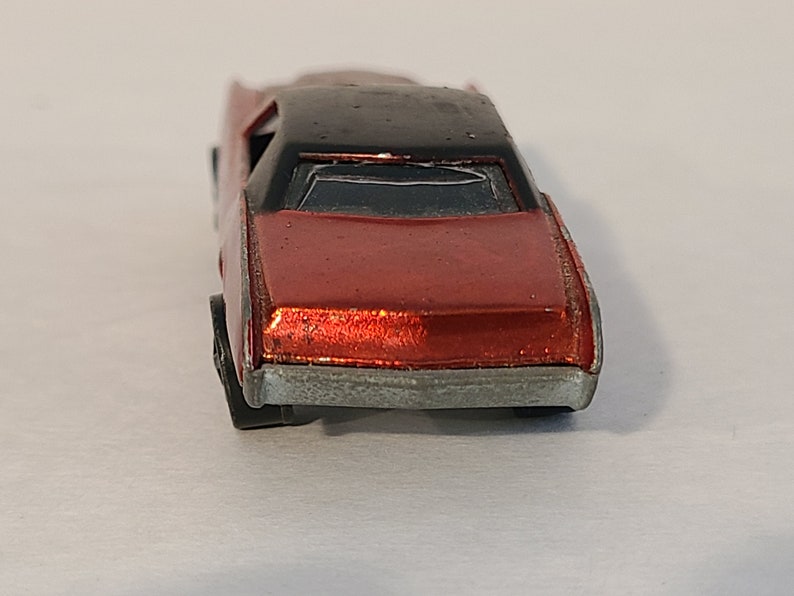 May include: A red toy car with a black roof and silver trim. The car is a vintage Hot Wheels model.