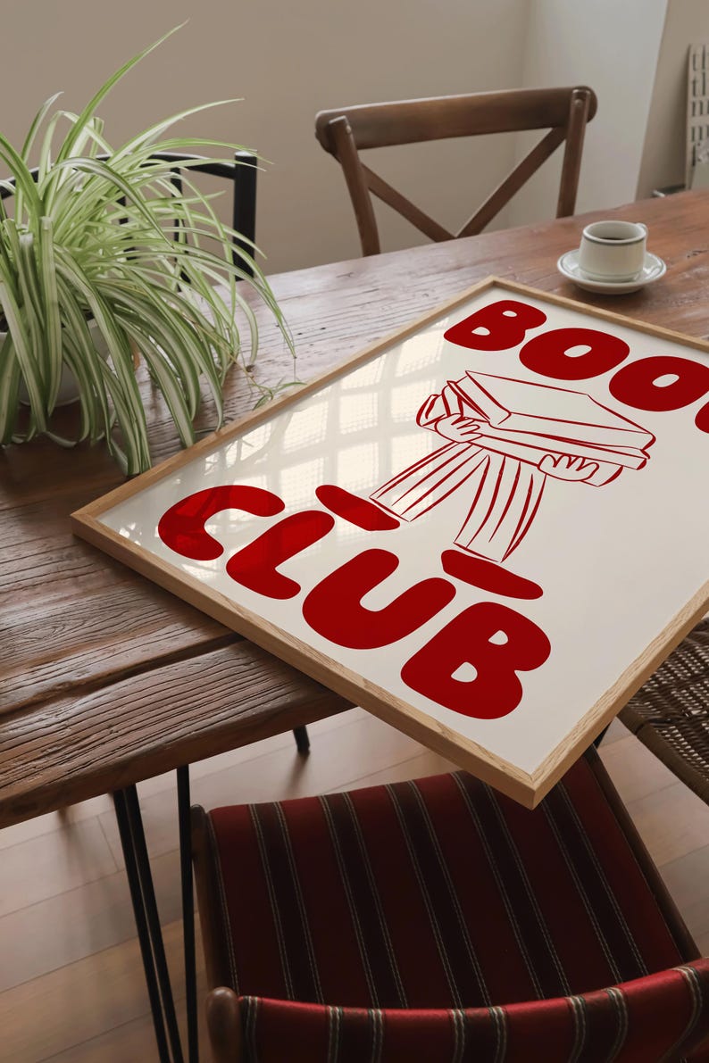 May include: A framed print featuring a red illustration of a person carrying a stack of books. The text "Book Club" is written in large red letters.