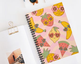 Puede incluir: Un cuaderno de espiral con un patrón repetitivo de frutas de dibujos animados que incluyen piñas, fresas, plátanos, limones y rodajas de sandía, todas con gafas de sol en forma de corazón sobre un fondo rosa claro ondulado.