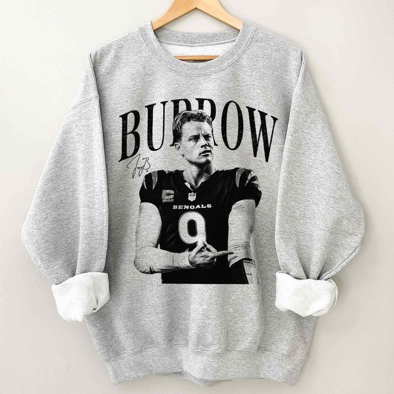 May include: A heather gray crewneck sweatshirt featuring a black and white graphic of a football player wearing a jersey with the number 9 and the word BENGALS. The name BURROW is printed in large black letters above the player, with a signature below.