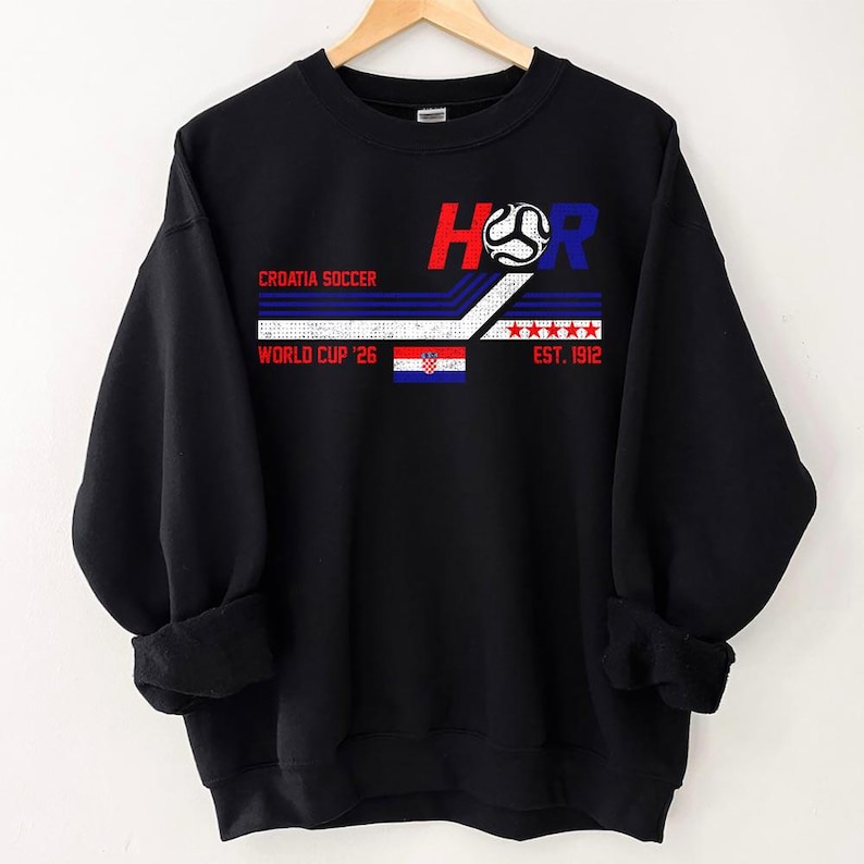 May include: Black sweatshirt with a graphic design featuring the text "HR" in red and blue, a soccer ball, and the Croatian flag. The text "CROATIA SOCCER" and "WORLD CUP '26" are also displayed. The sweatshirt has a crew neck and long sleeves.