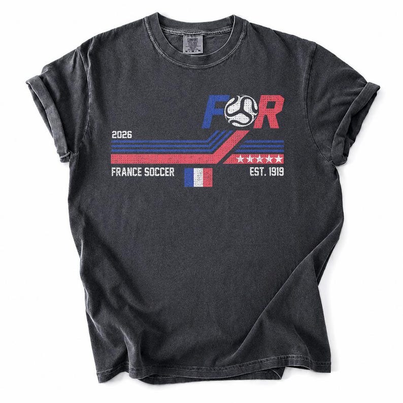 May include: Dark gray t-shirt with a graphic design. The design includes the text "FOR" with a soccer ball, "2026", "FRANCE SOCCER", a French flag, and "EST. 1919". The design uses red, white, and blue colors.