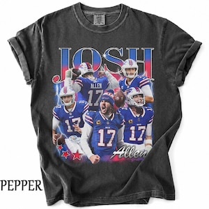 May include: A charcoal gray short-sleeve t-shirt featuring a graphic print of football player Josh Allen in various action poses wearing a blue Buffalo Bills uniform. The text JOSH and Allen appear in large stylized lettering with blue lightning.