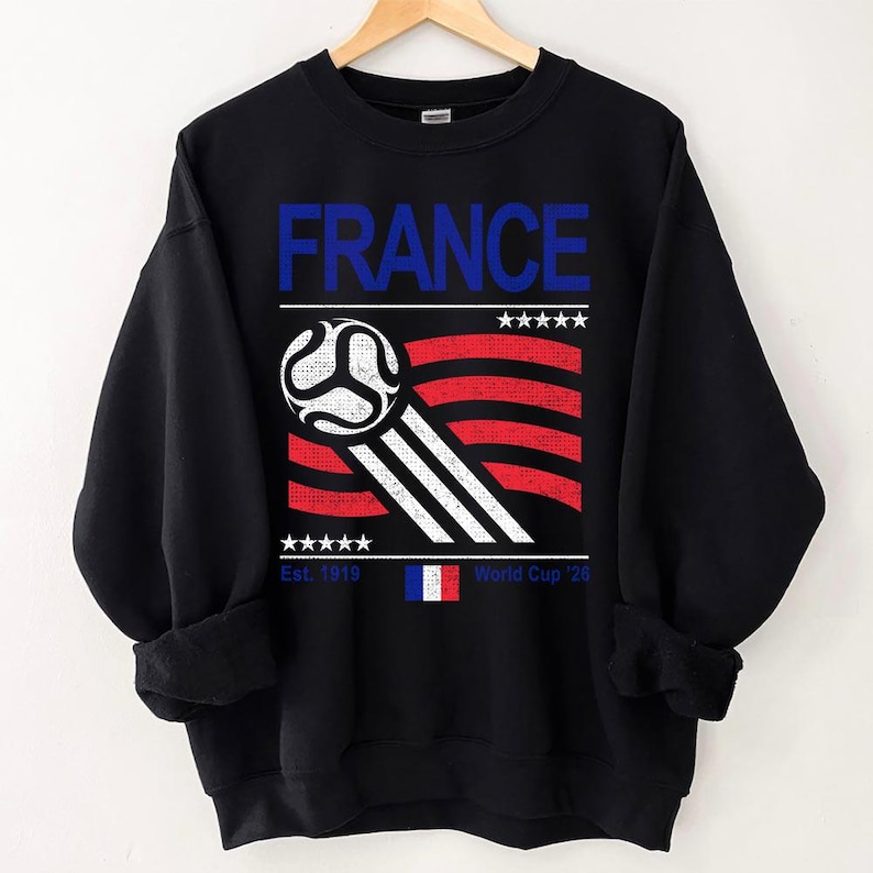 Pu&ograve; includere: Felpa nera con un design grafico con la scritta "FRANCE" in blu, un pallone da calcio e una bandiera francese stilizzata in rosso, bianco e blu. &Egrave; incluso anche il testo "Est. 1919" e "World Cup '26".