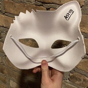 May include: White cat mask with elastic straps and the word 'ASTRO' written on the side.