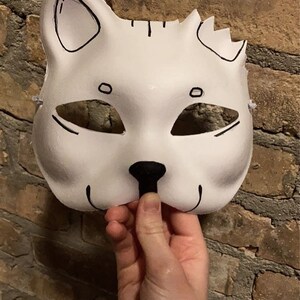 May include: A white cat mask with black eyes, nose, and whiskers. The mask has a simple design and is made of a lightweight material.