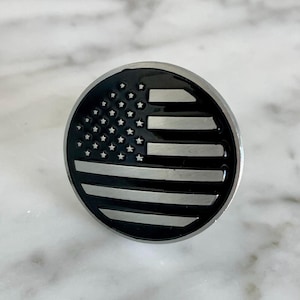 May include: A round, silver-colored pin with a black and white American flag design.