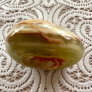May include: A smooth, green, brown, and white egg-shaped stone with swirling patterns.