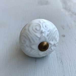May include: White ceramic knob with a decorative swirl pattern and a brass accent.