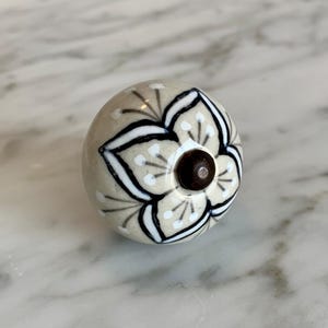 May include: A ceramic knob with a white and black floral design. The knob has a brown center.