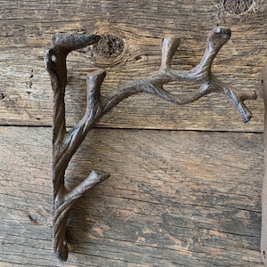 May include: A cast iron wall hook in the shape of a tree branch. The hook is a dark brown color and has a textured, rustic appearance. The branch has multiple offshoots, providing several points for hanging items. The hook is designed to be mounted on a wall.