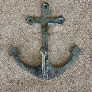 May include: A weathered, blue-green metal anchor hook with a cross-shaped top. The anchor is a decorative wall hook.